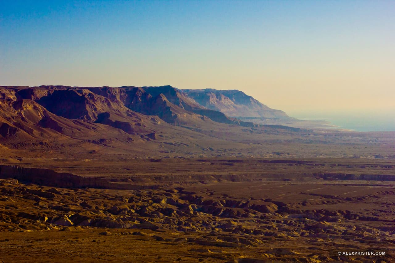 A broad desert valley and hard-cut plateau beneath a clear blue sky