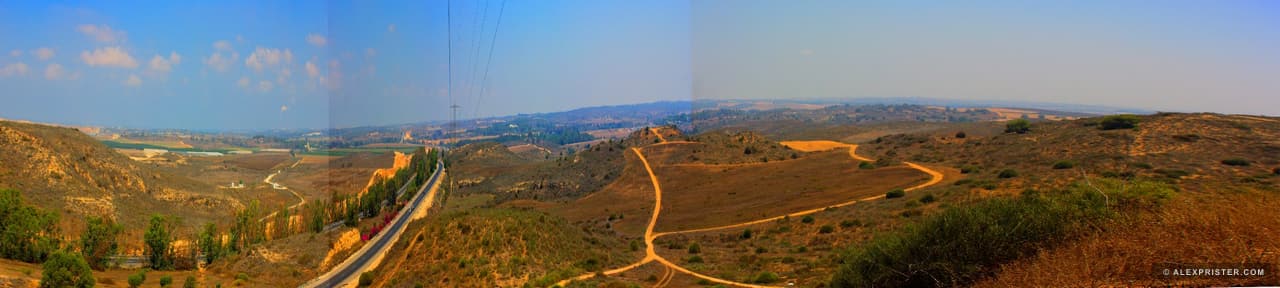 A panoramic road threading through green-brown hills toward the horizon